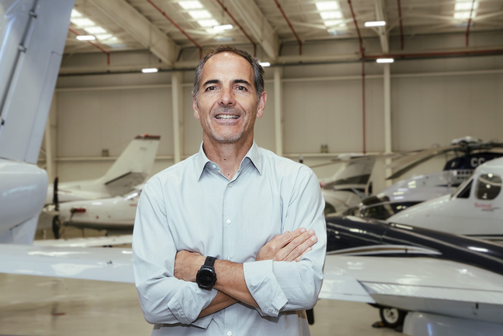 Rodrigo Contreras, CEO de Aviasur, de brazos cruzados en el hangar de la compañía en el aeropuerto de Santiago, con aviones de aviación ejecutiva y un helicóptero al fondo