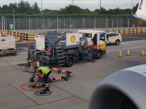 Operario conectando la manguera de un camión cisterna de combustible a un avión comercial en plataforma