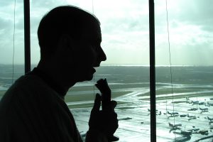 Controlador aéreo en la torre de control de un aeropuerto internacional, con la plataforma al fondo