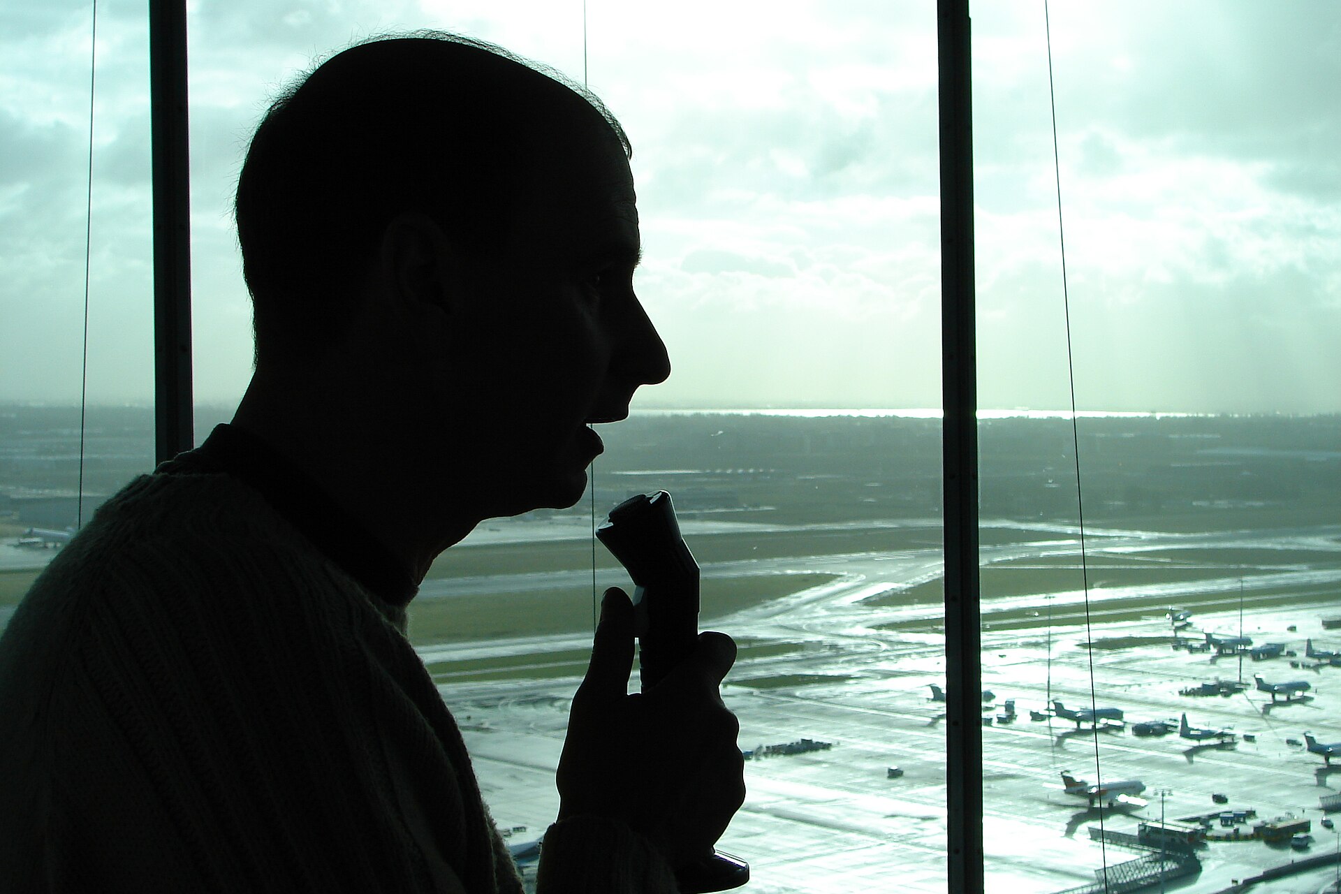Controlador aéreo en la torre de control de un aeropuerto internacional, con la plataforma al fondo